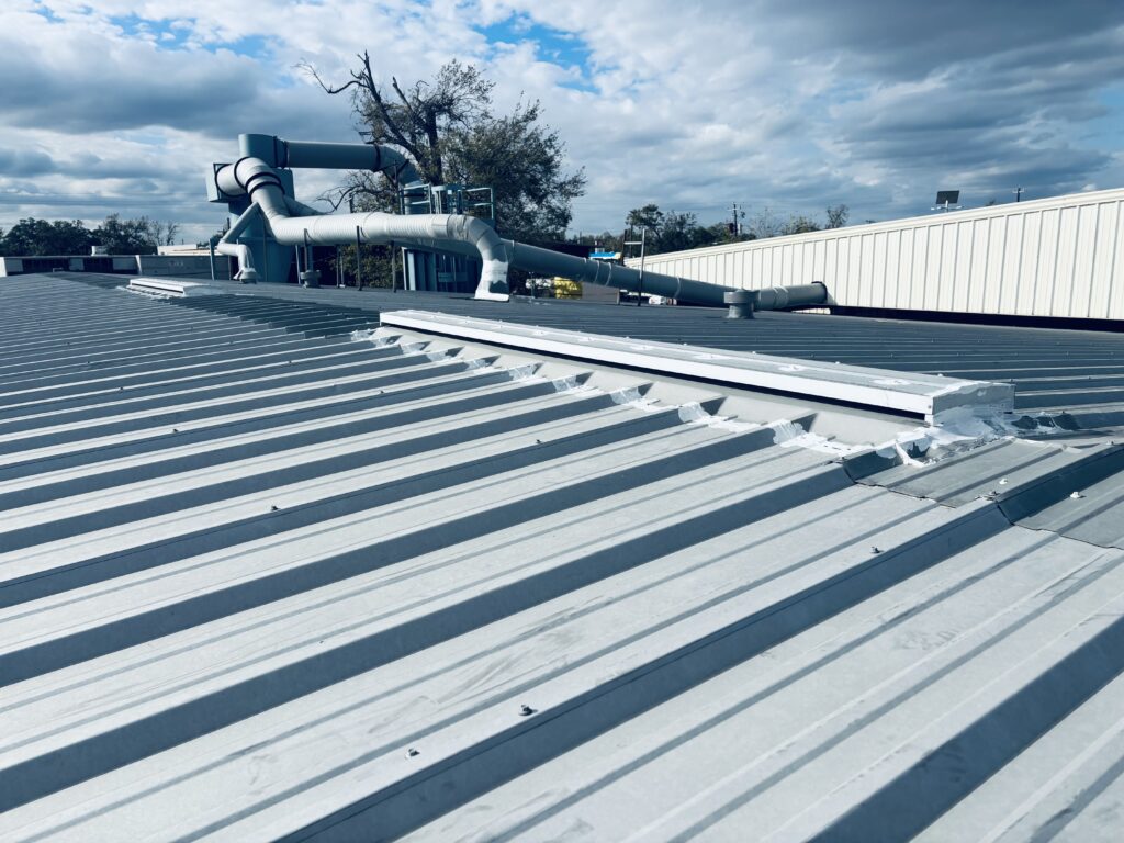 Corrugated metal roof with standing seam, featuring ventilation pipes and structural elements, showcasing repair work for enhanced durability and weather resistance in a commercial building.