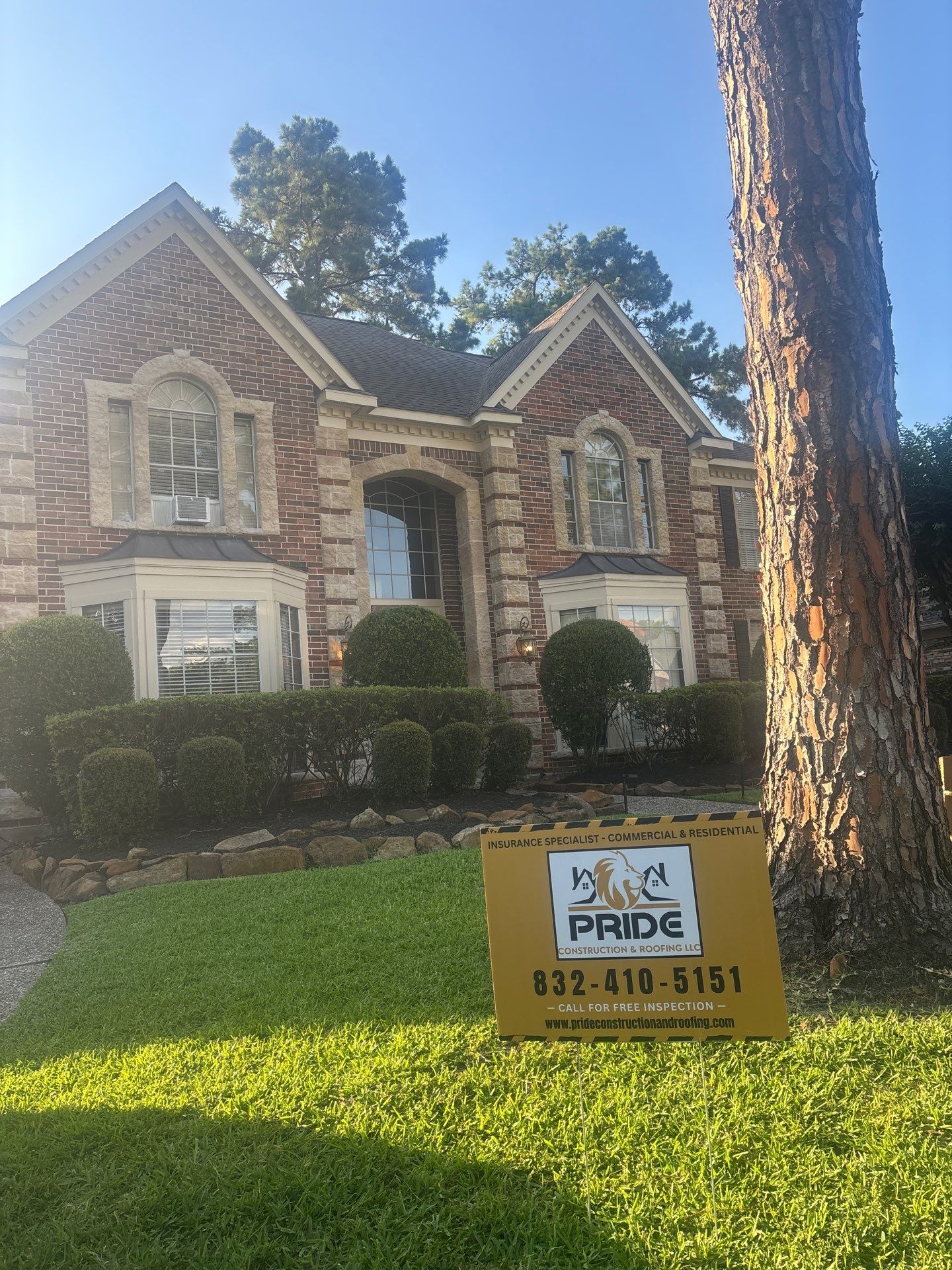 Elegant brick home with a well-maintained lawn, featuring a "Pride Construction & Roofing" sign in front, emphasizing residential services and free inspections.