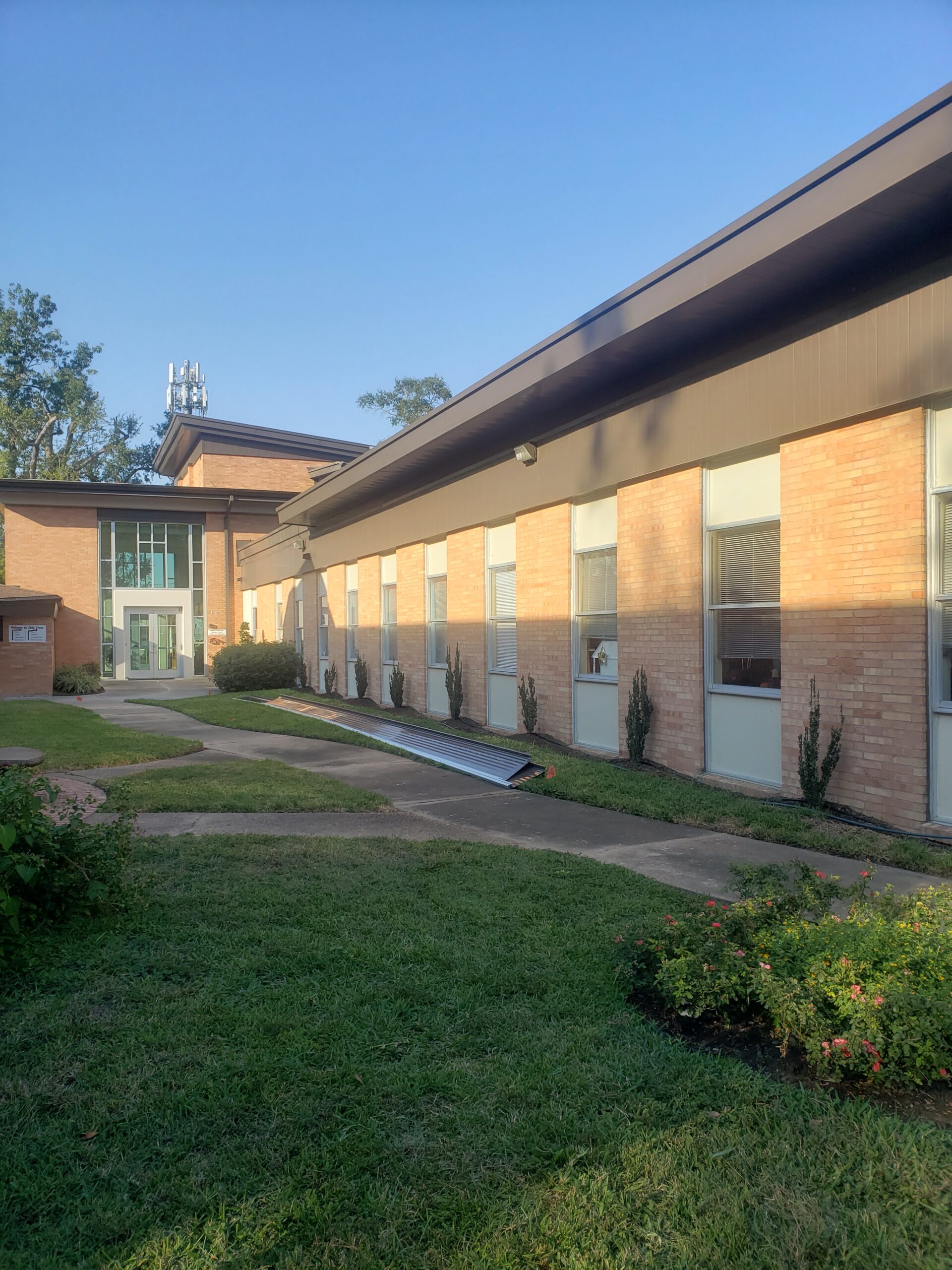 Church building in Houston's Spring Branch neighborhood with new standing seam roof, landscaped walkway, and metal roofing materials on the ground, showcasing commercial roofing services by Pride Construction & Roofing.