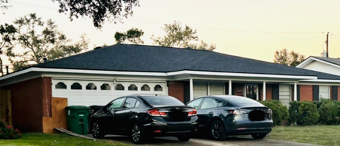 Residential home with a newly installed black asphalt shingle roof, parked cars in driveway, and well-maintained landscaping, showcasing Pride Construction & Roofing's remodeling expertise.