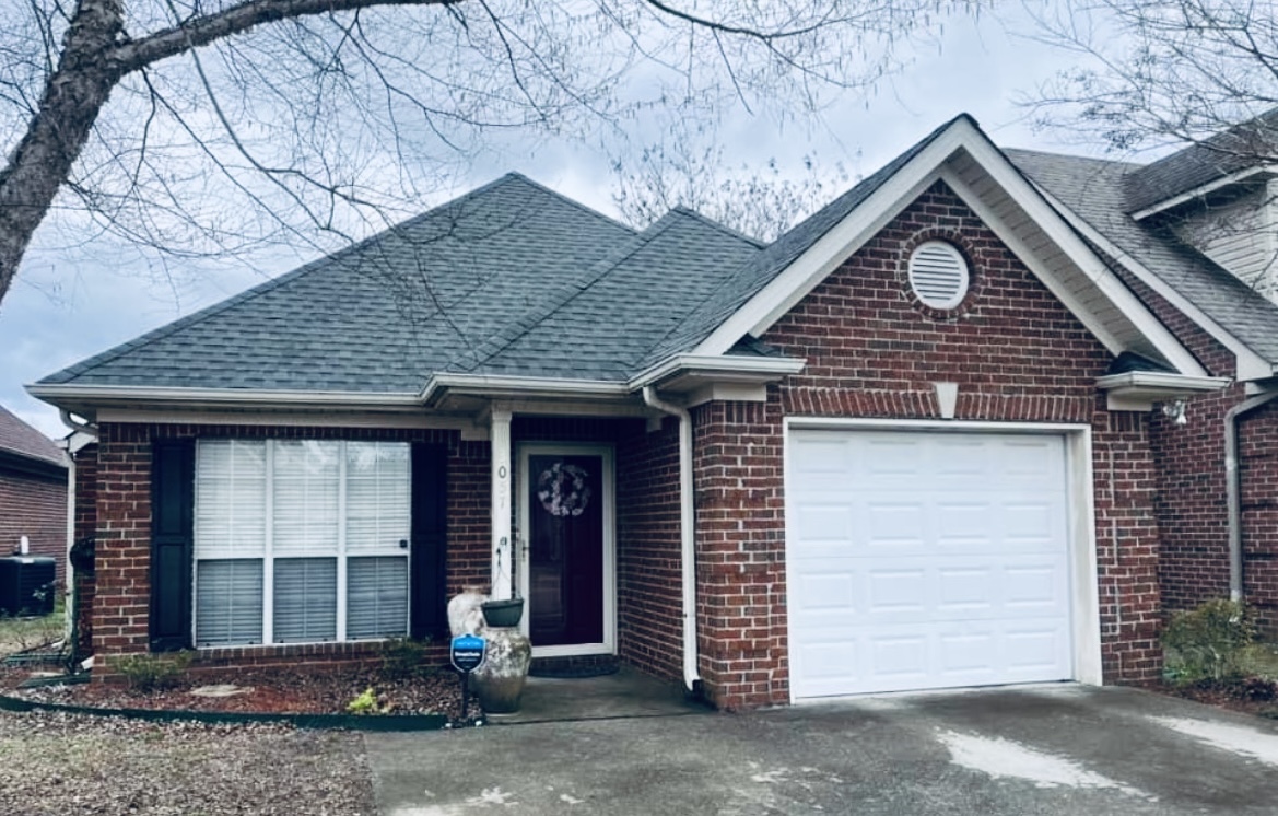 Brick home facade with a new roof, white garage door, and decorative front door, showcasing residential remodeling by Pride Construction & Roofing.