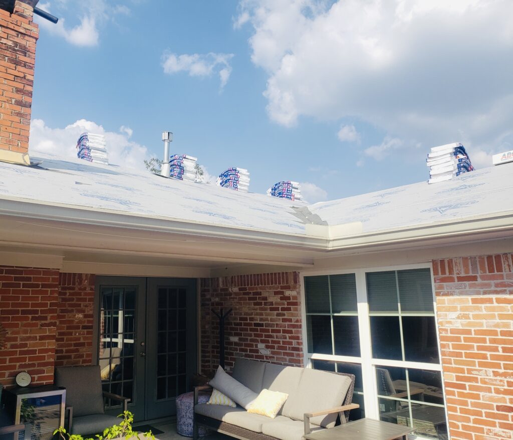 Roof under construction with stacked shingles and a cozy patio area, showcasing residential roofing services by Pride Construction & Roofing in Houston.