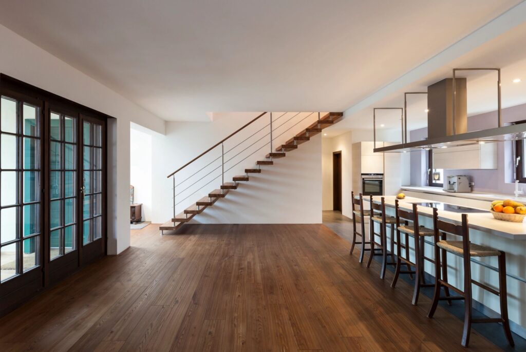 Modern open-concept kitchen and living area with wooden flooring, sleek cabinetry, and stylish staircase, showcasing luxury custom home design by Pride Construction & Roofing.