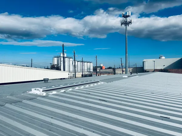 Roofing project showcasing a standing seam metal roof with clear blue sky, industrial buildings, and a cell tower in the background, highlighting Pride Construction & Roofing's craftsmanship in commercial roofing services.
