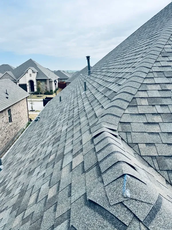 Roofing installation with asphalt shingles, showcasing detailed craftsmanship and structure, surrounded by residential homes in a suburban neighborhood.