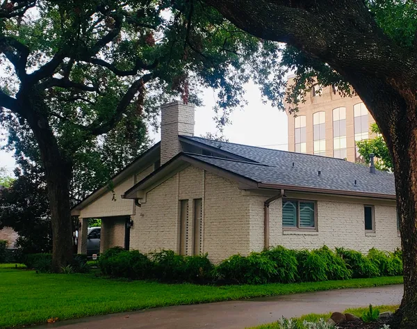 Residential home in Houston with new roofing, surrounded by greenery and trees, showcasing quality roofing services by Pride Construction & Roofing.