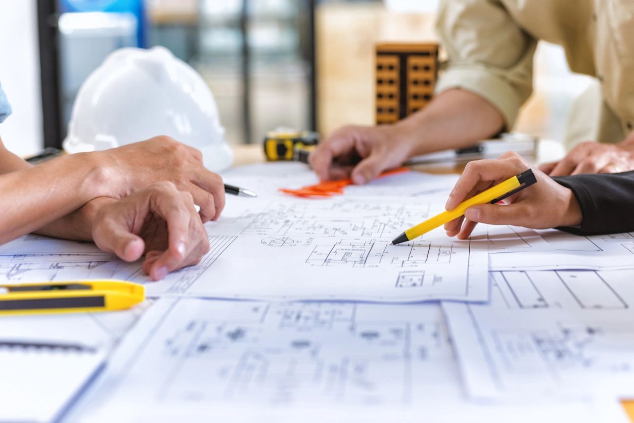 Hands collaborating over construction blueprints with a yellow pen, highlighting plans for quality construction and remodeling services at Pride Construction & Roofing.