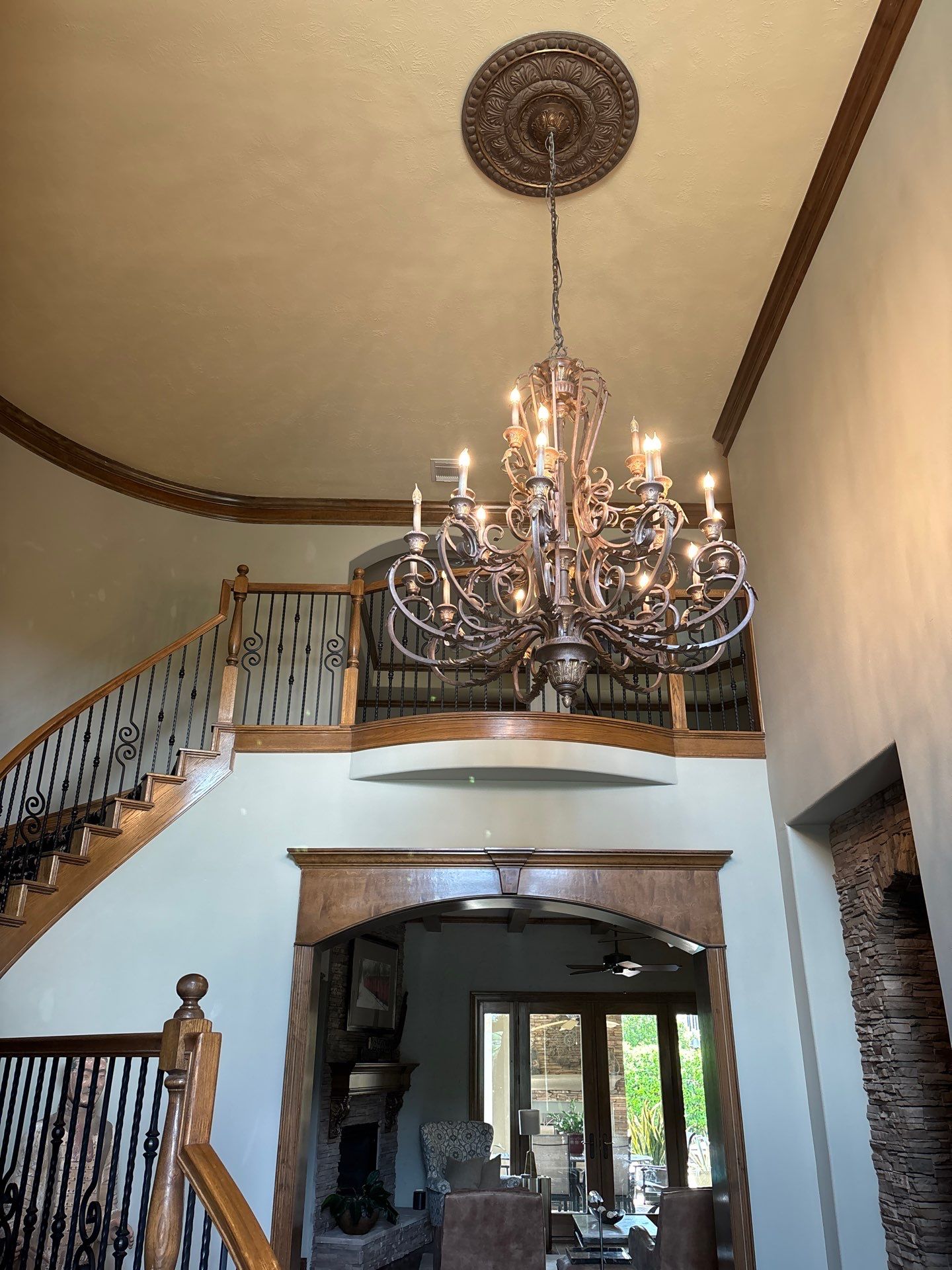 Chandelier hanging from the ceiling in an elegantly designed entryway with a curved staircase and decorative railings, showcasing the interior craftsmanship of Pride Construction & Roofing.