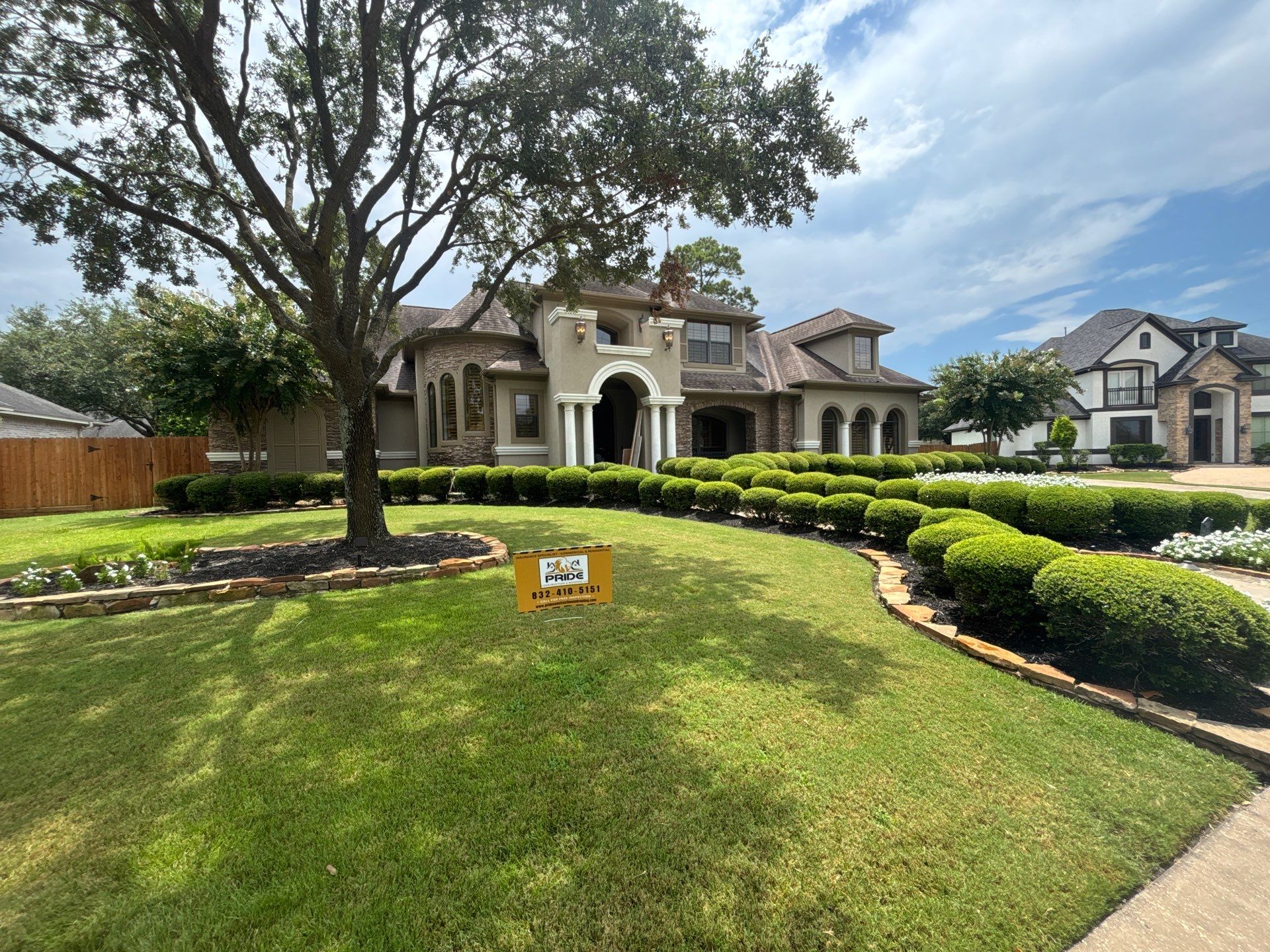 Luxury home exterior with manicured landscaping, including round hedges and flower beds, featuring a "Pride Construction" sign, showcasing residential remodeling and landscaping services in Houston Heights.