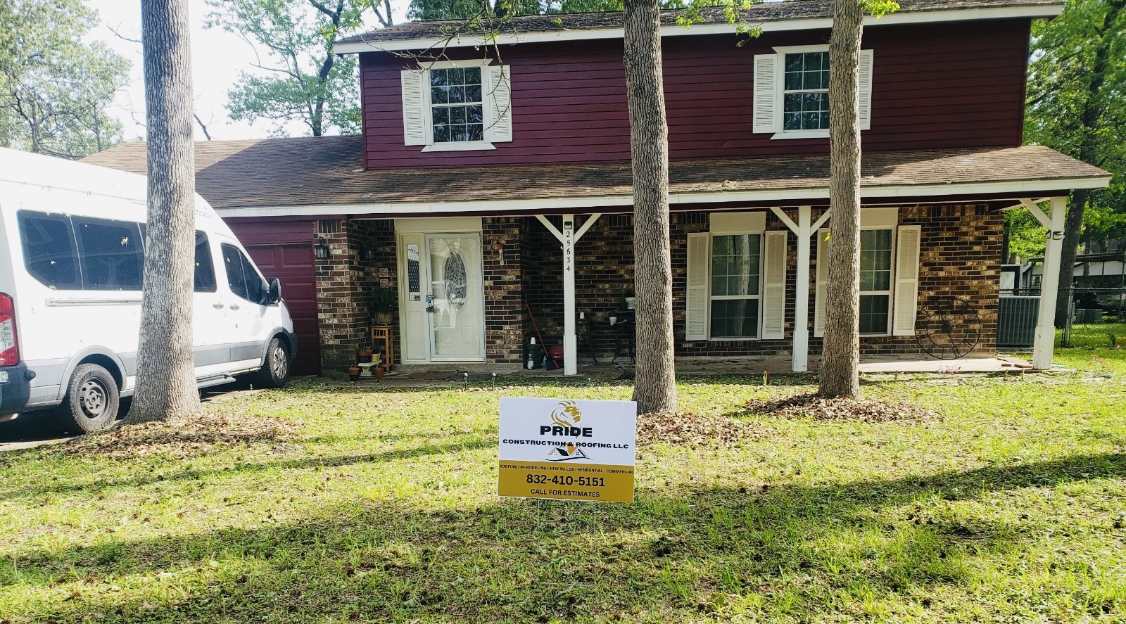 Front view of a two-story home with maroon siding and brick accents, featuring a lawn sign for Pride Construction & Roofing, showcasing their services for roofing and remodeling in Houston.