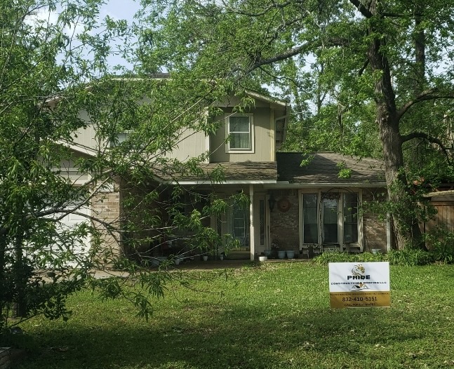 Pride Construction & Roofing renovated a two-story home in a lush, green setting, showcasing updated exterior features and a visible company sign.